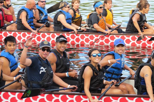 Paddlers in bright red boats on the water, smiling and posing for the camera.