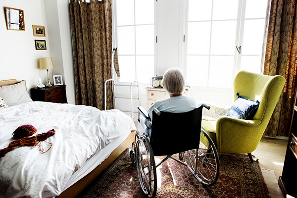 person in wheelchair looks out the window, elder in an eldercare facility with a lack of nurses present.
