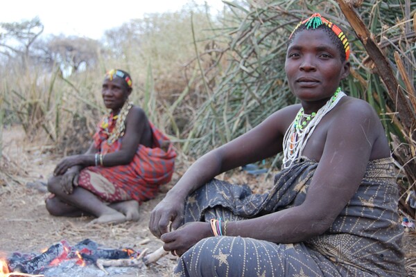 Two people in traditional Tanzanian clothing sitting on the ground outdoors.