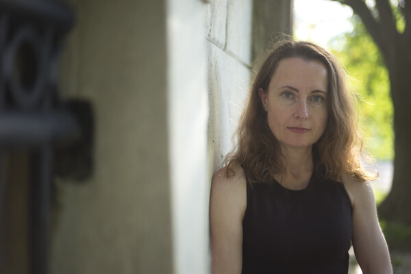 Professor leaning against a stone wall with a tree behind her.