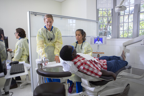 Two Penn Dental students provide dental care to a patient in a dental chair.