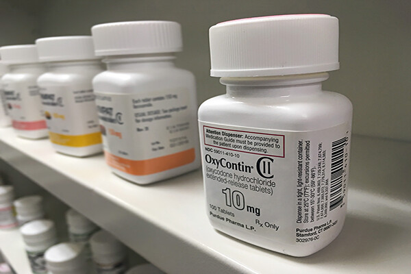 shelf of prescription bottles, focused on one bottle of OxyContin.
