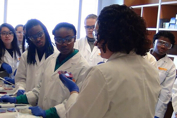 high school students in lab coats face an instructor in a reproductive science lab.