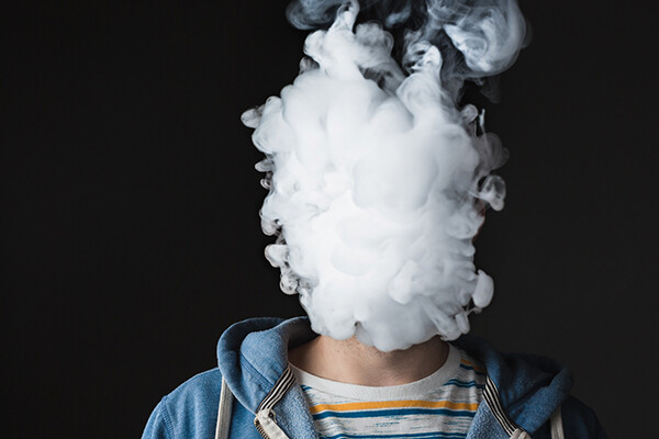 Cloud of e-cigarette vapor engulfs the face of a teenager in a sweatshirt
