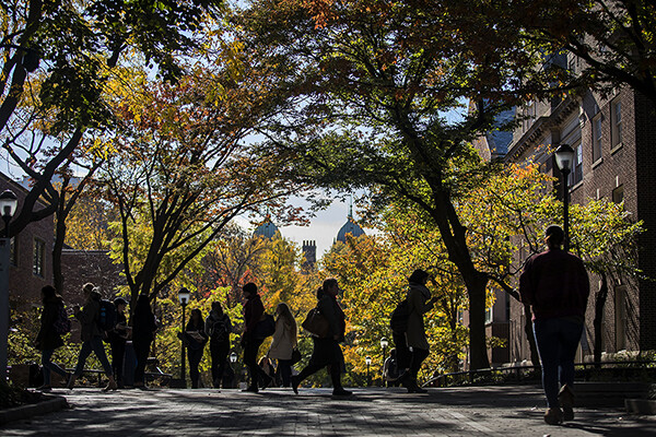 Pedestrians on Penn campus in the autumn sun with fall leaves.