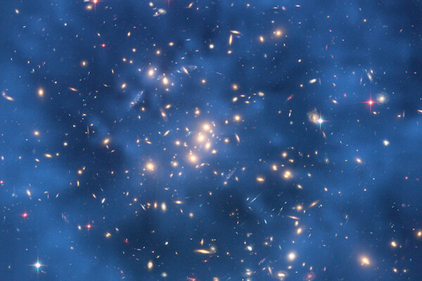 a cluster of galaxies shown against a dark blue background, a faint darker ring can be seen around the center of the image