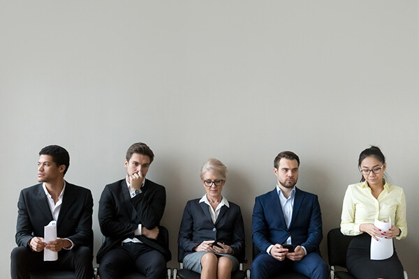 Five people sitting in chairs against a wall wearing suits waiting for a job interview.