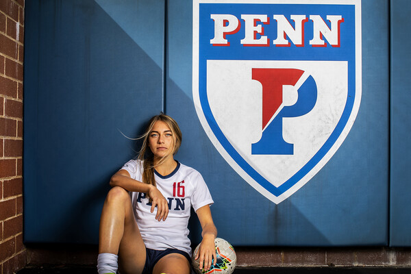 Breukelen Woodard of the women's soccer team poses sitting down near a Penn shield at Rhodes Field.
