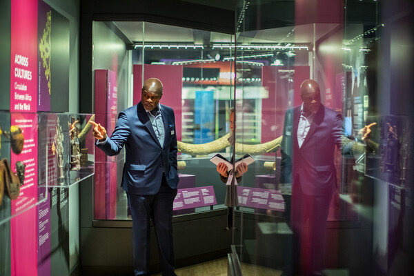 Man in a suit pointing to a glass box containing artifacts