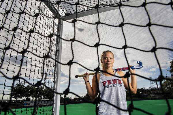At Ellen Vagelos Field, Alexa Schneck of the field hockey team poses on the field hockey field in a net with her stick across her shoulders.