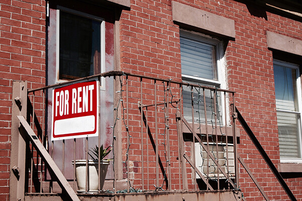 For Rent sign on front gate of a brick apartment building