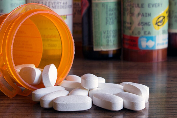 closeup of prescription pill container on its side with white oblong pills spilling out.