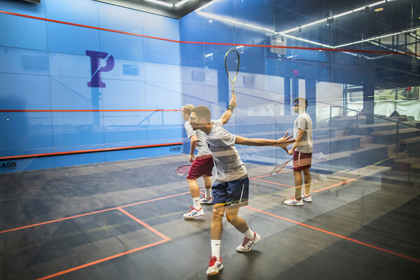 Inside one of the fancy new glass courts at Penn's revitalized Penn Squash Center, three men play squash.