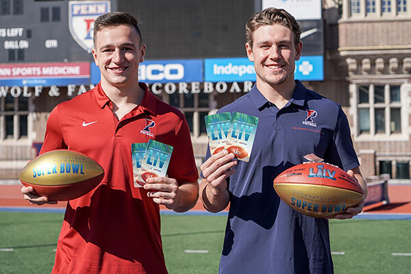 Anthony Lotti and Sam Philippi hold tickets to the Super Bowl in one hand and footballs in the other on a football field.