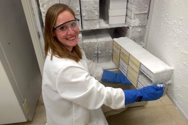 Veterinary scientist in lab coat, gloves and goggles smiles while handling frozen biological samples