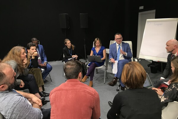 Group of people sitting in a circle, with an easel and paper next to the group.