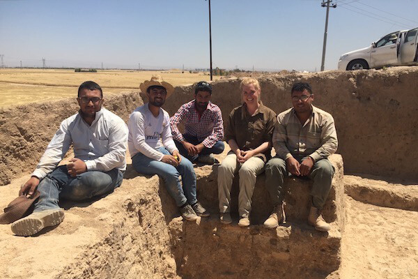 Five people sit along ancient mud walls at an archeological dig in Iraq.