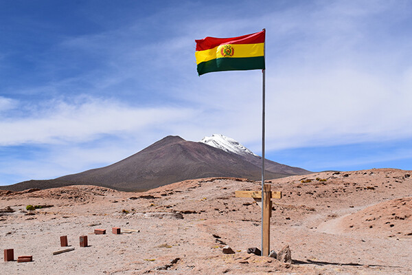 Bolivian flag flying on high rocky terrain with mountain peaks in background
