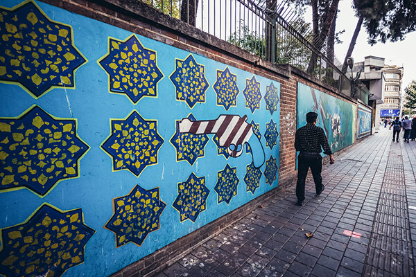 Pedestrian on the sidewalk walking past the wall of the former US embassy in Tehran.