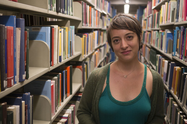 A person standing in a library stack, with shelves of books on either side. 