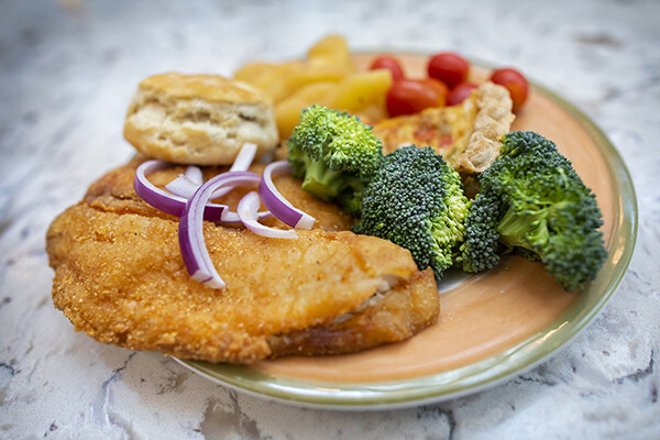 Plate of food with fried fish, crab pie, butter biscuit, broccoli, and tomatoes.