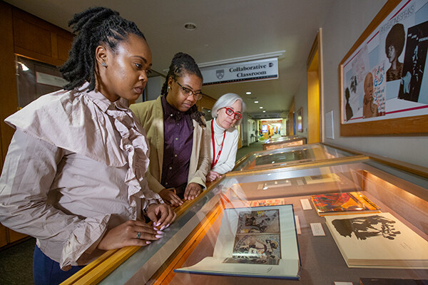 Two grad students and library curator looking at Joanna Banks Exhibit