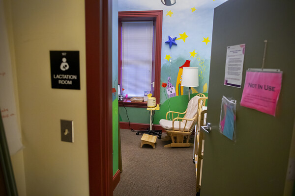 Sign outside an open door reads Lactation Room, opened door reveals a rocking chair, lamp, brightly painted walls and a breast pump.