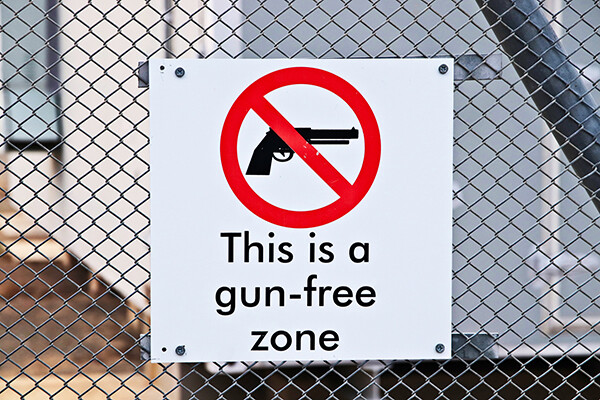 Sign on a chain-link fence reads "This is a gun-free zone."