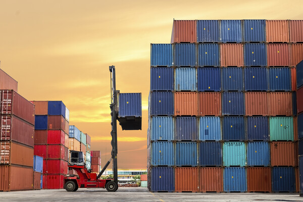 Colorful shipping containers piled high, with one being loaded by a truck. 