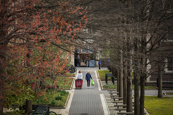 Two people walk through Locust Walk, one pushing a move-out cart.
