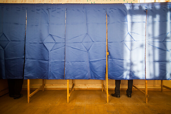 One person voting behind a curtain in one of a row of three voting booths