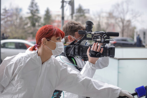 A reporter and a cameraman wear protective clothing and masks while reporting on the coronavirus from the field.
