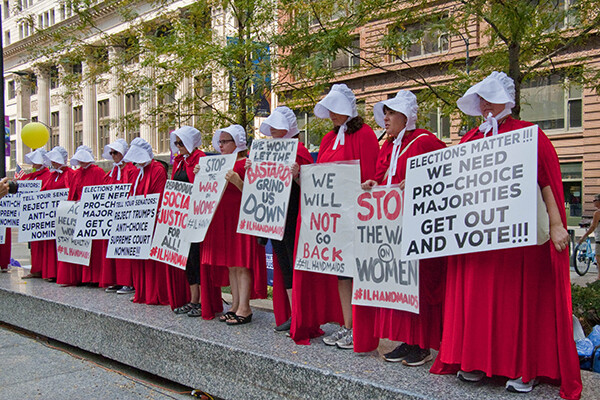 Line of protesters dressed as characters from The Handmaid’s Tale holding protest signs
