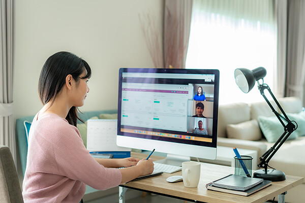 a person sits at a desktop computer at home watching a work video conference