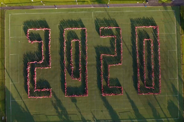 Bird's eye view of Penn Park with member of the class of 2020 standing on bright green grass and spelling out the number 2020 in an outline font.