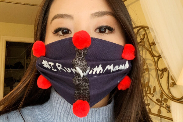 student wearing a dark mask with pom-poms with words #IRunWithMaud