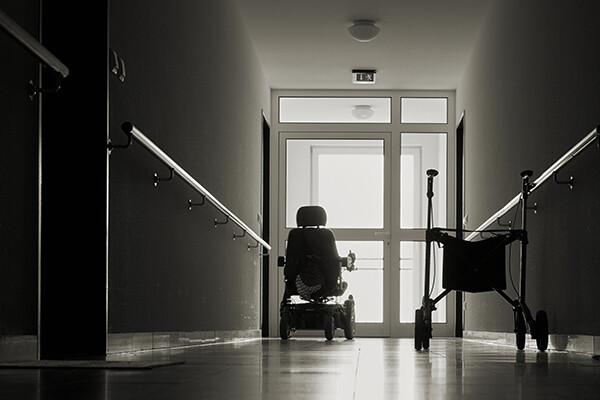Empty hallway in a nursing home with an electric wheelchair and a walker by a sunlit door