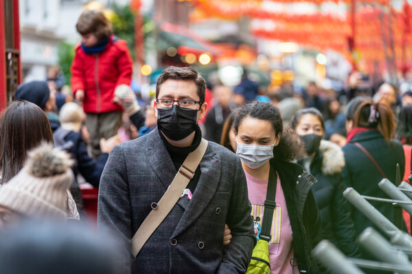 Not practicing social distancing, people walk down the street in close quarters wearing masks.