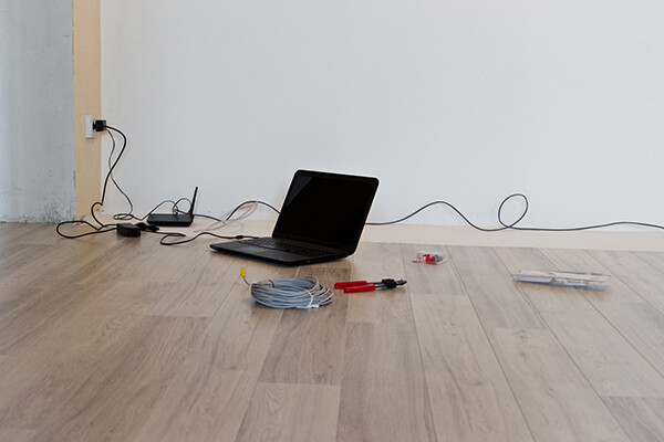 laptop on the floor of an empty room with cable, pliers and other tools for hooking up internet router and modem.