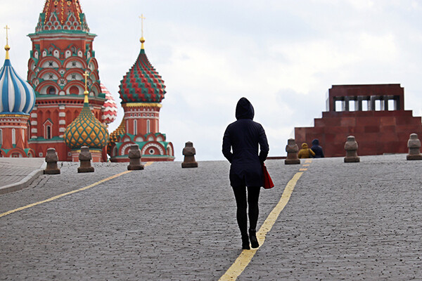 Person in black hooded jacket and pants facing away from camera walks near Red Square in Moscow.