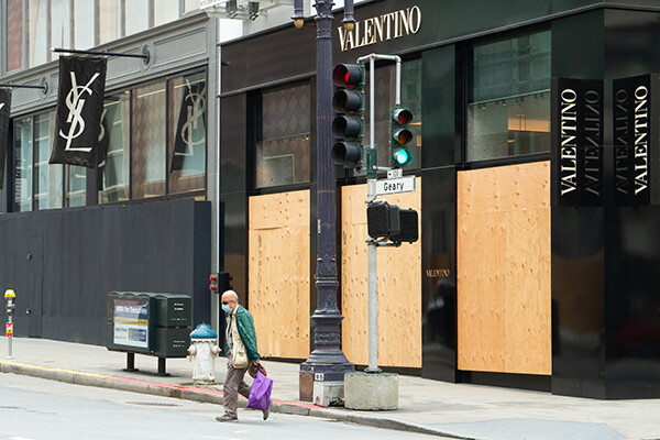 Person crosses at an intersection wearing a protective face mask in front of a boarded up Valentino storefront