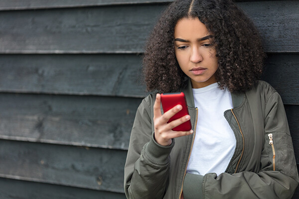A teenager looks critically at a smartphone in their hand