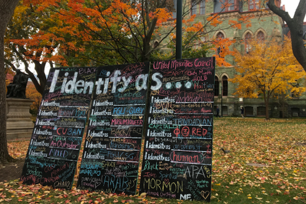 Three blackboards in front of Claudia Cohen Hall say "I identify as..." with various descriptors written in colorful chalk (mormon, human, FGLI, queer, etc)