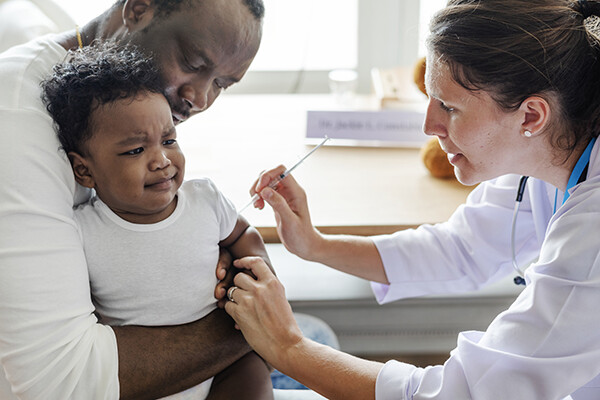 A doctor gives a baby a vaccine while the child’s parent holds them.