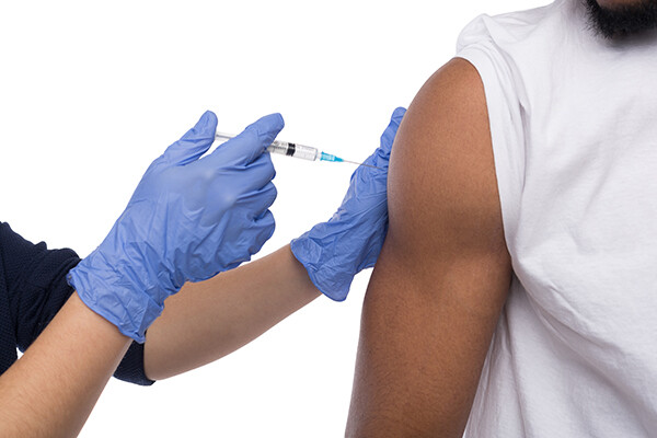 A gloved hand administers a vaccine to a person’s upper arm. 