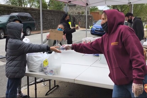 Children receive food from people working at a table wearing masks