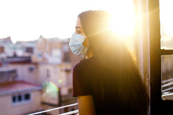 Masked young woman staring out of window