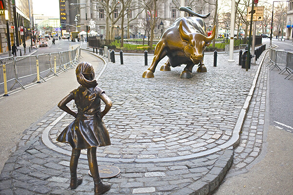 Fearless Girl bronze statue on Wall Street standing in front of the bull statue.