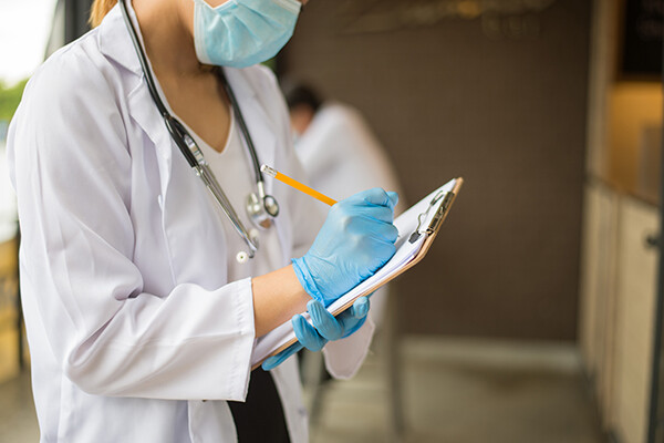 Doctor with a face mask and gloves writing with a pencil on a clipboard.