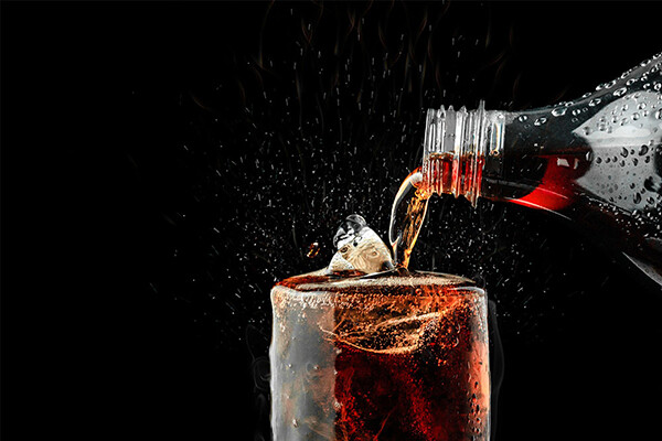 Closeup of a bottle of cola being poured into a glass with ice.